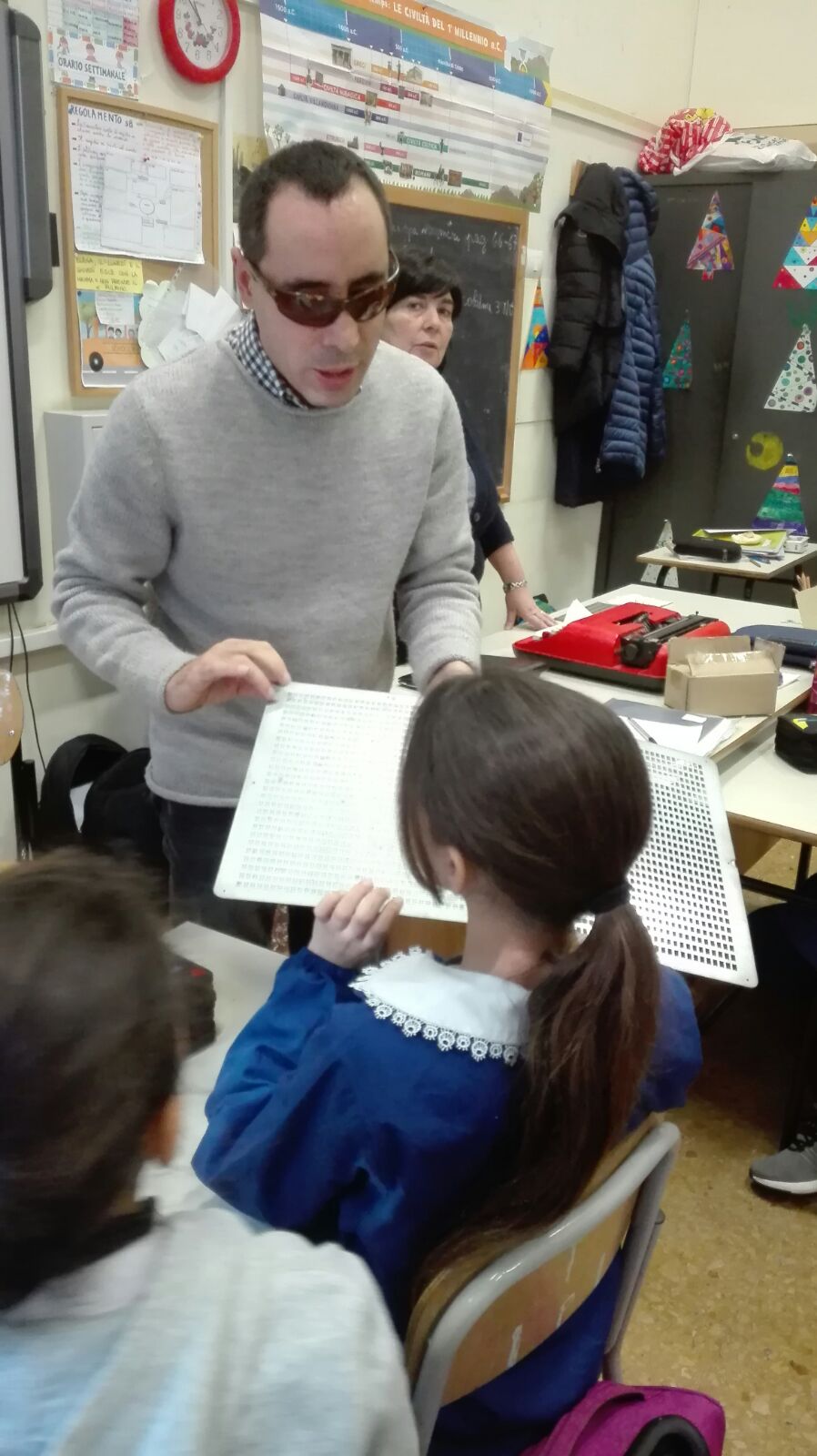 L'immagine Alessio Conti che spiega come utilizzare un libro tattile ad un'alunna della quinta elementare